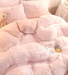 a bed with pink fluffy comforters and pillows on top of it, next to a teddy bear