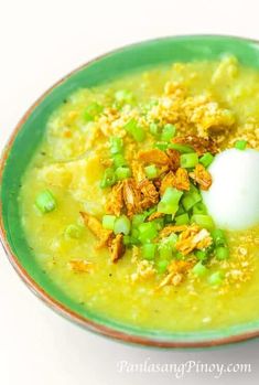 a green bowl filled with soup topped with sour cream and chopped green onions next to a spoon