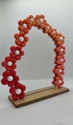 an orange and red sculpture with white balls on it's sides, sitting on a wooden stand