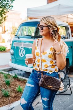 a woman walking down the street carrying a purse and holding a coffee in her hand