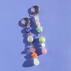 two pairs of earrings with charms attached to them on a blue surface, one has a skull and the other is a flower