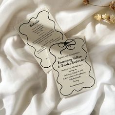 two wedding cards sitting on top of a white sheet