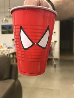 a person holding up a red cup with eyes painted on the side and one eye drawn on the inside