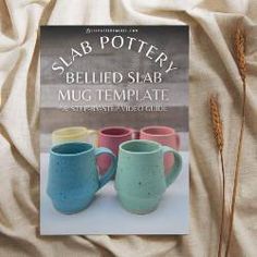 a book about pottery sitting on top of a bed next to some dry grass and two mugs