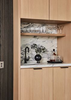 a kitchen with marble counter tops and wooden cabinets, filled with wine glasses on the shelves