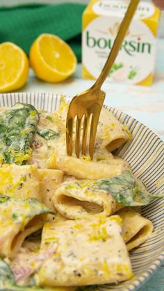 a fork is stuck into some pasta with spinach and lemons in the background