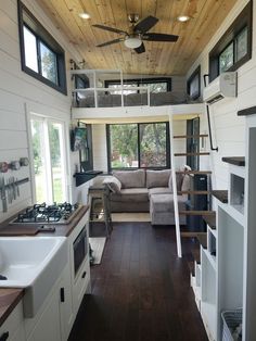 the interior of a tiny home with wood flooring and white walls, windows, and ceiling fan