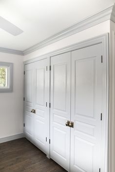 an empty room with white closets and wood flooring in front of a window