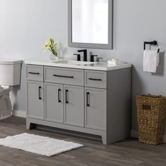 a white toilet sitting next to a bathroom sink under a mirror on top of a wooden floor