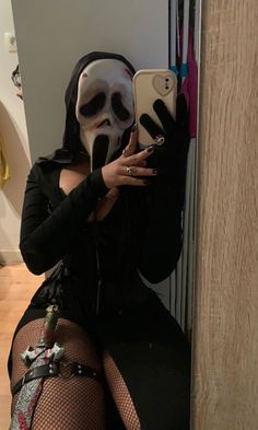 a woman wearing a mask and holding a cell phone in front of her face while sitting on the floor