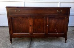 an old wooden cabinet with two doors and three drawers on the bottom, sitting in front of a garage door