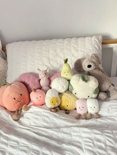 several stuffed animals are arranged on a bed with white sheets and pillows, all in different colors