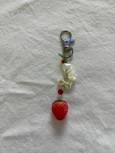 a key chain with a strawberry and flower charm hanging from it's side on a white cloth