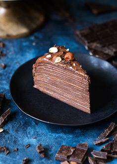 a piece of chocolate cake on a black plate next to pieces of chocolate and nuts