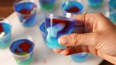 a hand holding a small glass filled with blue and red liquid