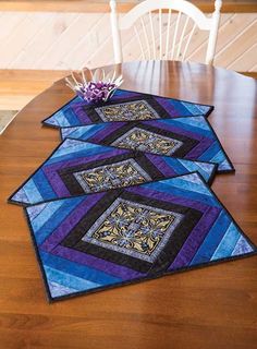 three quilted placemats sitting on top of a wooden dining room table next to a potted plant