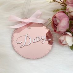 a pink ornament with the word daisy on it next to flowers and petals