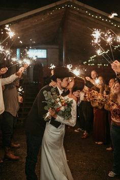 a bride and groom kiss as they hold sparklers in front of their wedding party