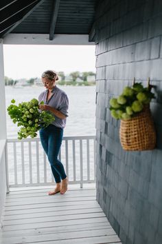 a woman standing on a porch holding a bunch of green vegetables and looking at her cell phone