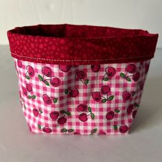 a pink and white checkered fabric basket with cherries on the front, sitting on a table