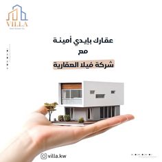 a hand holding a small model house in front of a white background with arabic writing