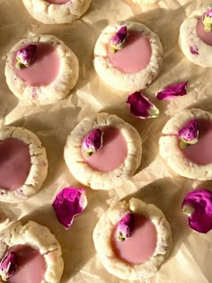 several cookies with pink icing and rose petals on them sitting on wax paper next to each other