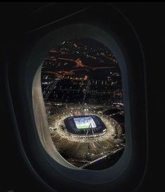 an airplane window with the view of a stadium from it's seat area at night