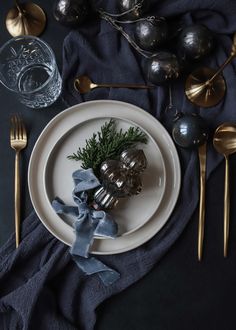 a white plate topped with silverware on top of a blue table cloth next to gold utensils