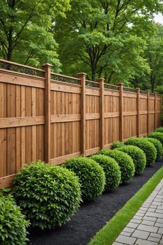 a wooden fence surrounded by green bushes and black mulch on the side of a brick walkway