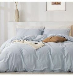 an unmade bed with blue sheets and pillows on top of it in a white room