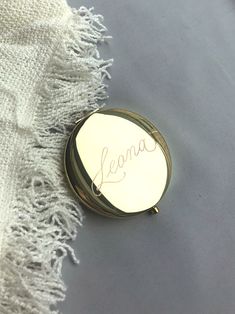 a compact mirror with the word jenny written in cursive writing on it sitting on a blanket