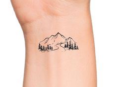 a small tattoo on the wrist of a woman with mountains and trees in the background