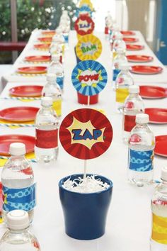 a table set up with water bottles, plates and cupcakes for a super hero birthday party