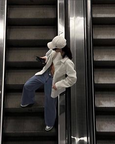 a woman is standing on an escalator and looking at her cell phone while wearing a white hat