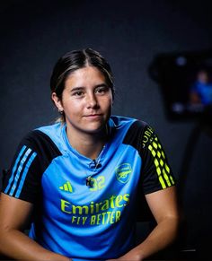 a woman sitting at a table in front of a camera and wearing a blue shirt