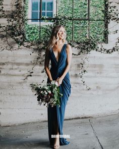 a woman standing in front of a window holding a bouquet and wearing a blue dress