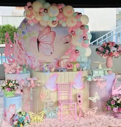 an outdoor display with balloons, flowers and butterflies on the side of the stage at a children's birthday party