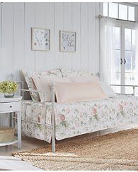 a white bed sitting next to a window in a room with flowers on the bedspread