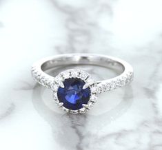 One of a kind round blue sapphire center surrounded by a sparkling diamond halo The perfect pop of color for when you decide to pop the question It's the perfect way to pop the question! A ring made for a princess - this gorgeous setting features a royal blue sapphire surrounded by a halo of sparkling diamonds. We love how dainty and feminine this ring is. It is a modern twist on the classic engagement ring. Perfect for the modern bride. It can serve both "something new and something blue" on yo Round Blue Sapphire Ring, Classic Engagement Ring, Classic Engagement, Blue Sapphire Ring, The Modern Bride, Ring With Diamond, Sparkling Diamond, Classic Engagement Rings, Blue Sapphire Rings