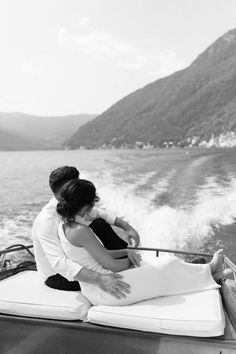 a man and woman sitting on the back of a boat in front of a body of water