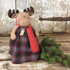 a stuffed moose with a red scarf on it's neck sitting next to pine cones