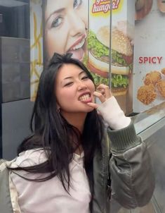 a woman standing in front of a fast food restaurant holding her finger up to her mouth