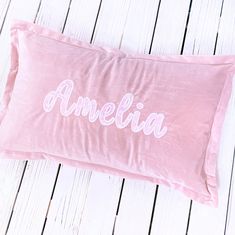 a pink pillow with the word amelie on it sitting on a white wooden floor next to a pair of scissors