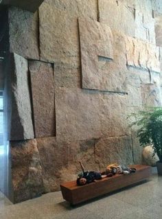 a stone wall in an office building with some plants on the floor and other decorations