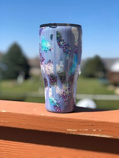 a purple and blue cup sitting on top of a wooden table next to a window