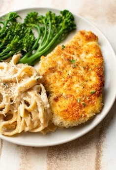 a white plate topped with meat and pasta next to broccoli on a table