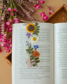 an open book sitting on top of a table next to flowers and a wicker basket