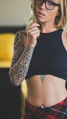 a woman wearing glasses and a black top with tattoos on her arms is posing for the camera