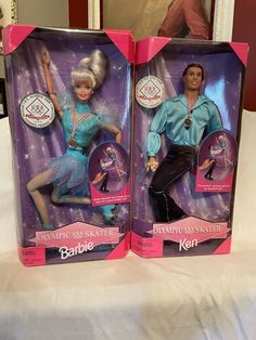 two barbie dolls in their packaging on a bed