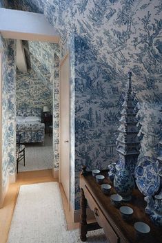 a hallway with blue and white wallpaper, vases on the table and an open door leading to another room